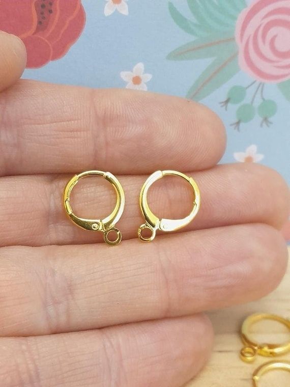 To små guldfarvede ringlåse til smykkefremstilling holdes mellem fingre